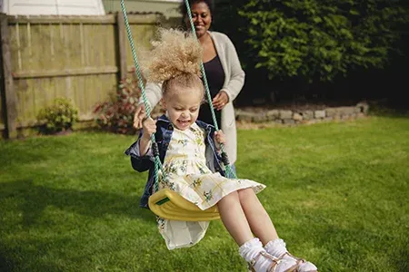Mother pushing daughter on swing in back yard